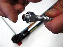 A person holding a nut and screw with a pair of pliers in the background.